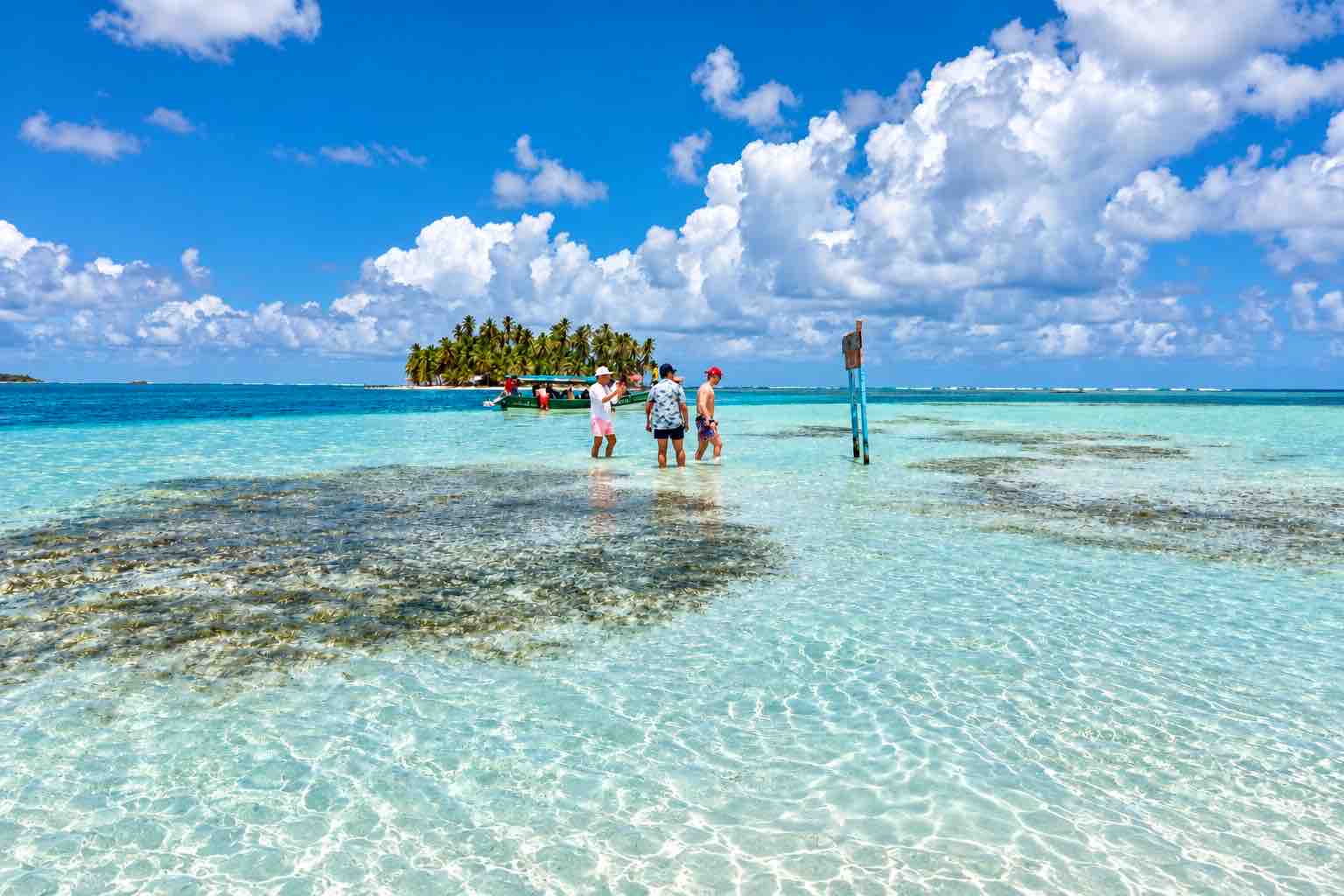Shallow San Blas Natural Pool sandbar with visitors and a palm-covered island in the distance