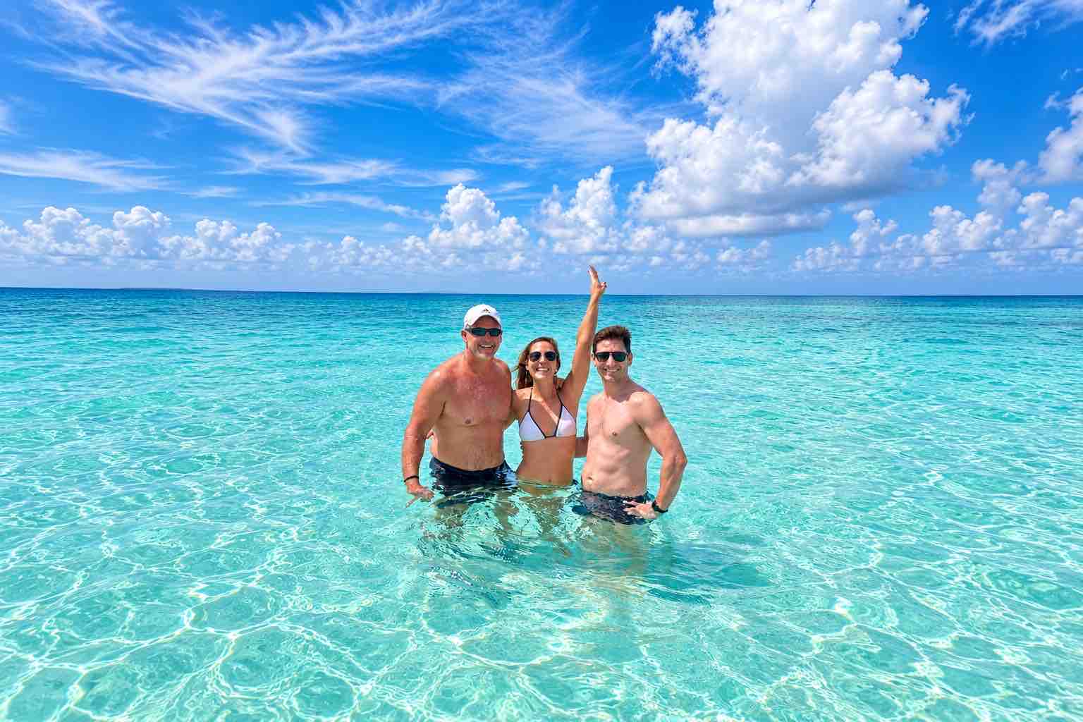 Three guests smiling together in waist-deep turquoise water at the San Blas Natural Pool
