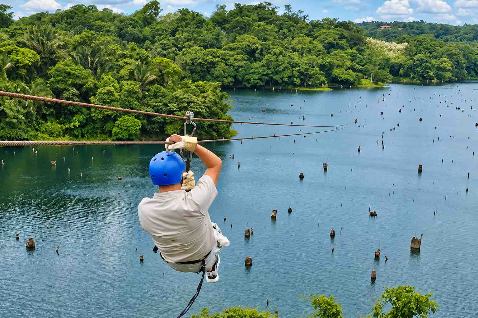 Guest in a blue helmet riding above water with a forested shoreline on the Zipline Panama tour