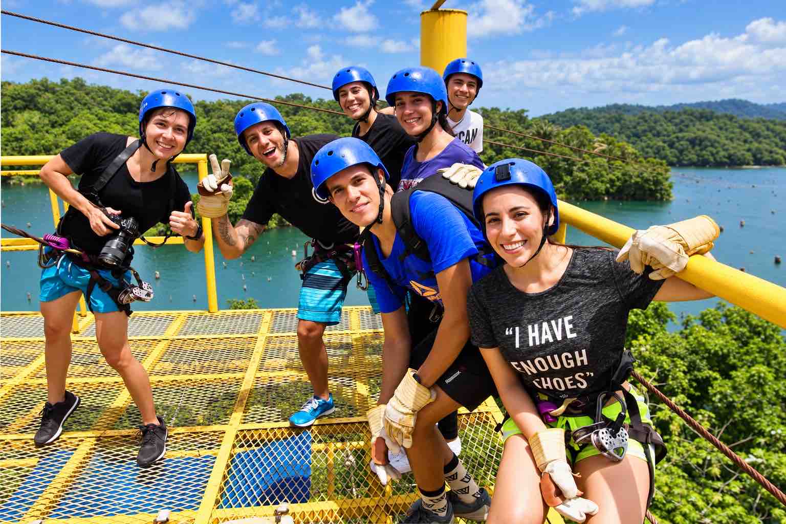 Smiling guests in blue helmets posing on a yellow platform above water during the Zipline Panama tour