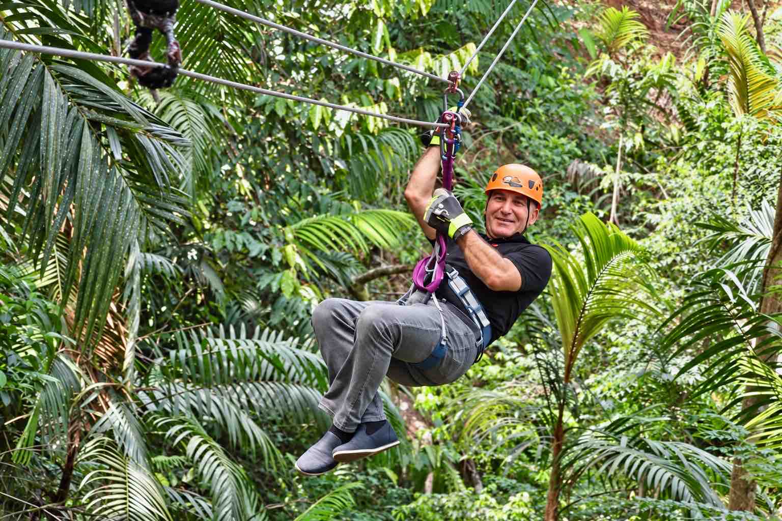 Man in an orange helmet and harness riding among palms on the Zipline Panama tour