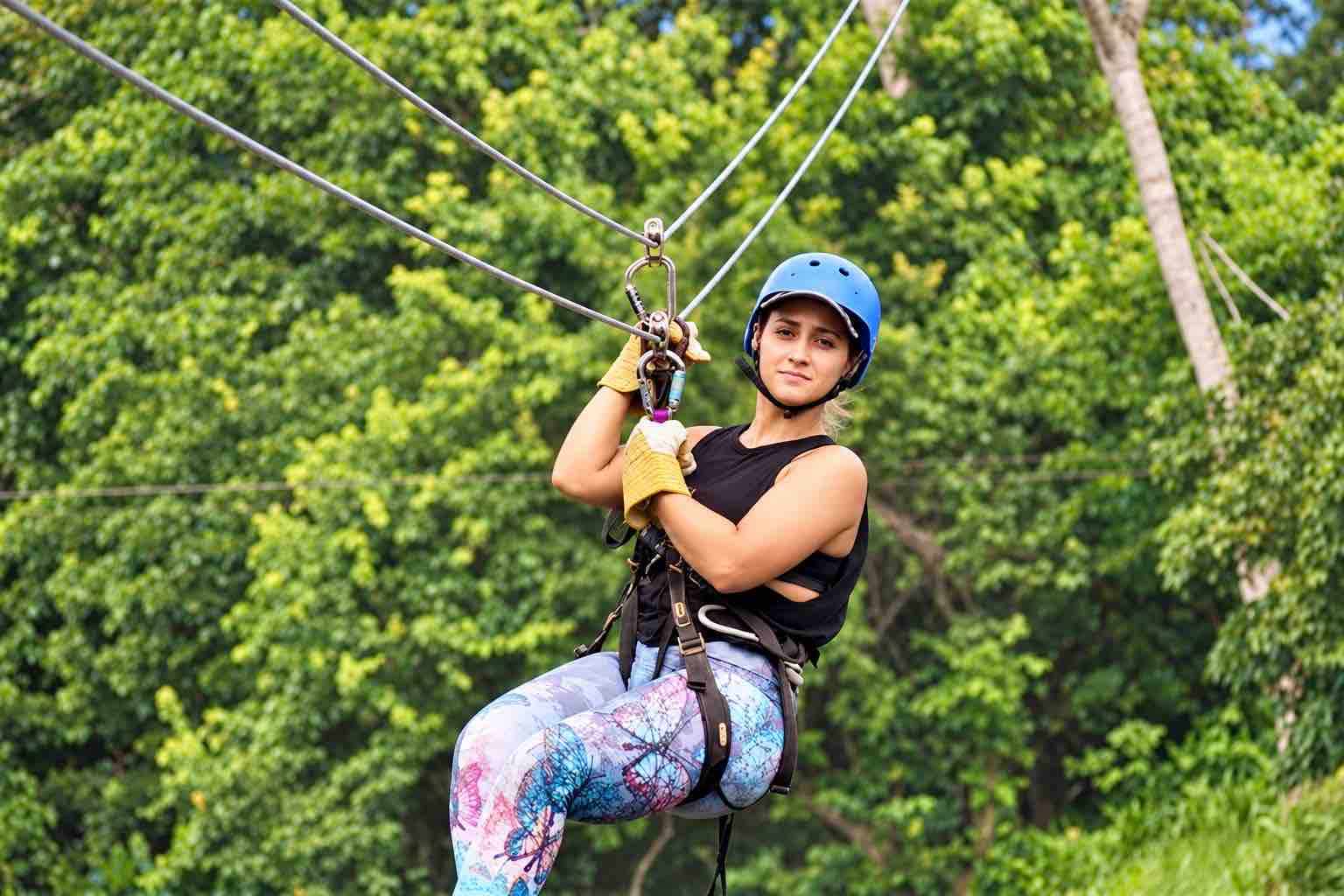 Woman wearing a blue helmet and harness suspended against a green forest backdrop on the Zipline Panama tour