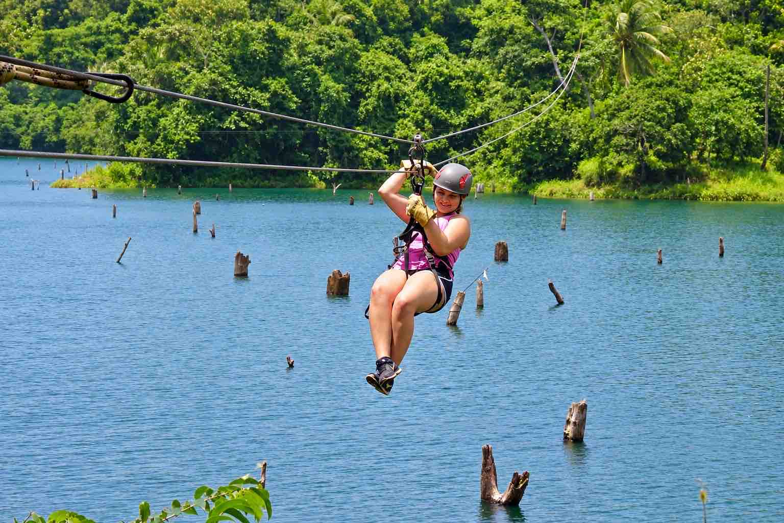 Woman wearing a helmet and harness riding above water on the Zipline Panama tour