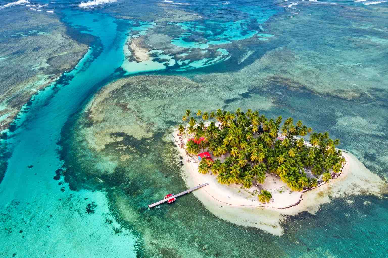 Aerial view of a palm-covered San Blas island, boat dock, and surrounding reef