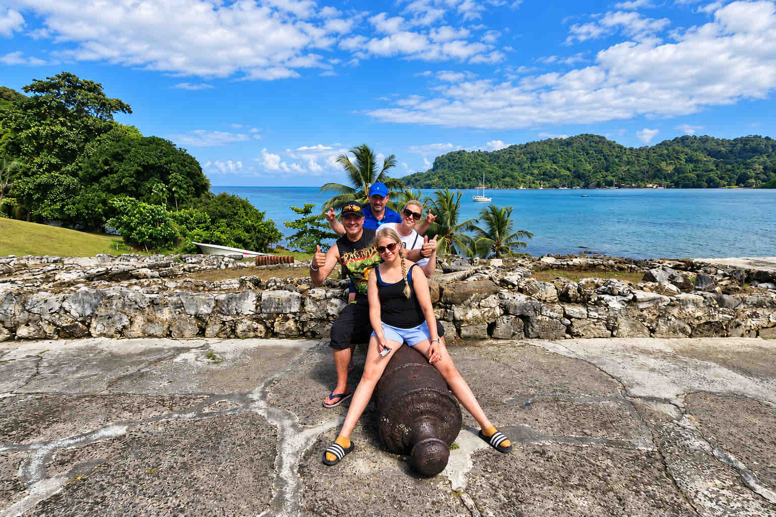 Guests posing on a historic cannon overlooking the bay on a Panama Canal Shore Excursion from Colón