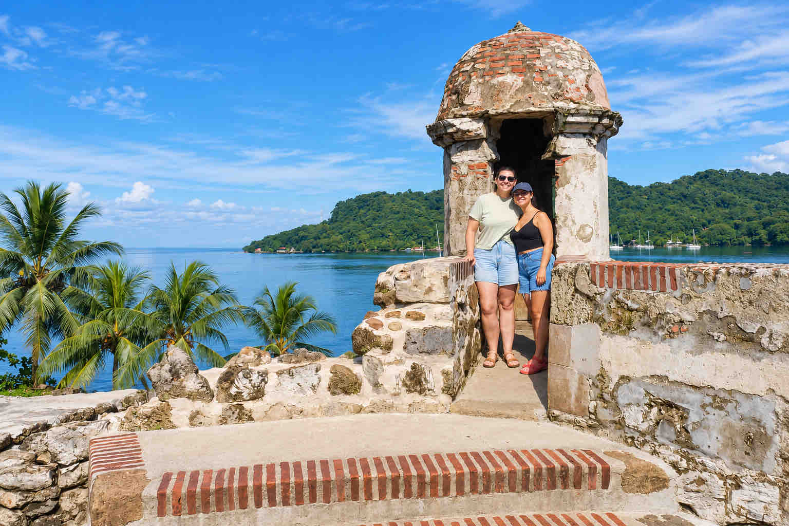 Two guests posing beside a historic sentry box by the sea on a Panama Canal Shore Excursion from Colón