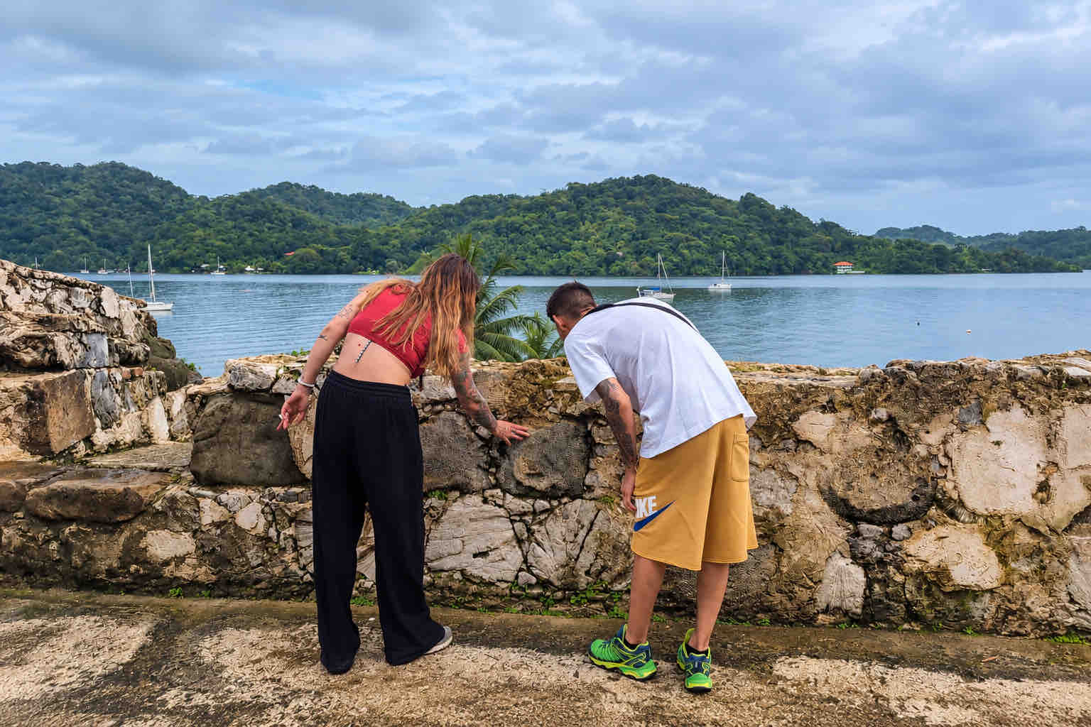 Two guests examining a historic stone wall beside the bay on a Panama Canal Shore Excursion from Colón