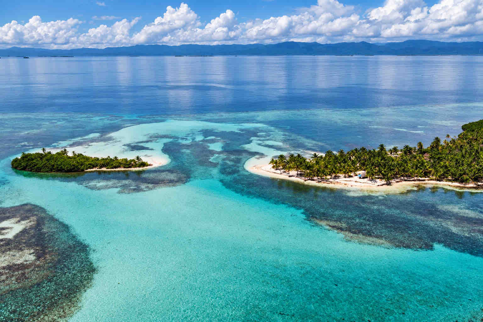 Aerial view of palm-covered islands and turquoise reef shallows in Cayos Holandeses, San Blas.