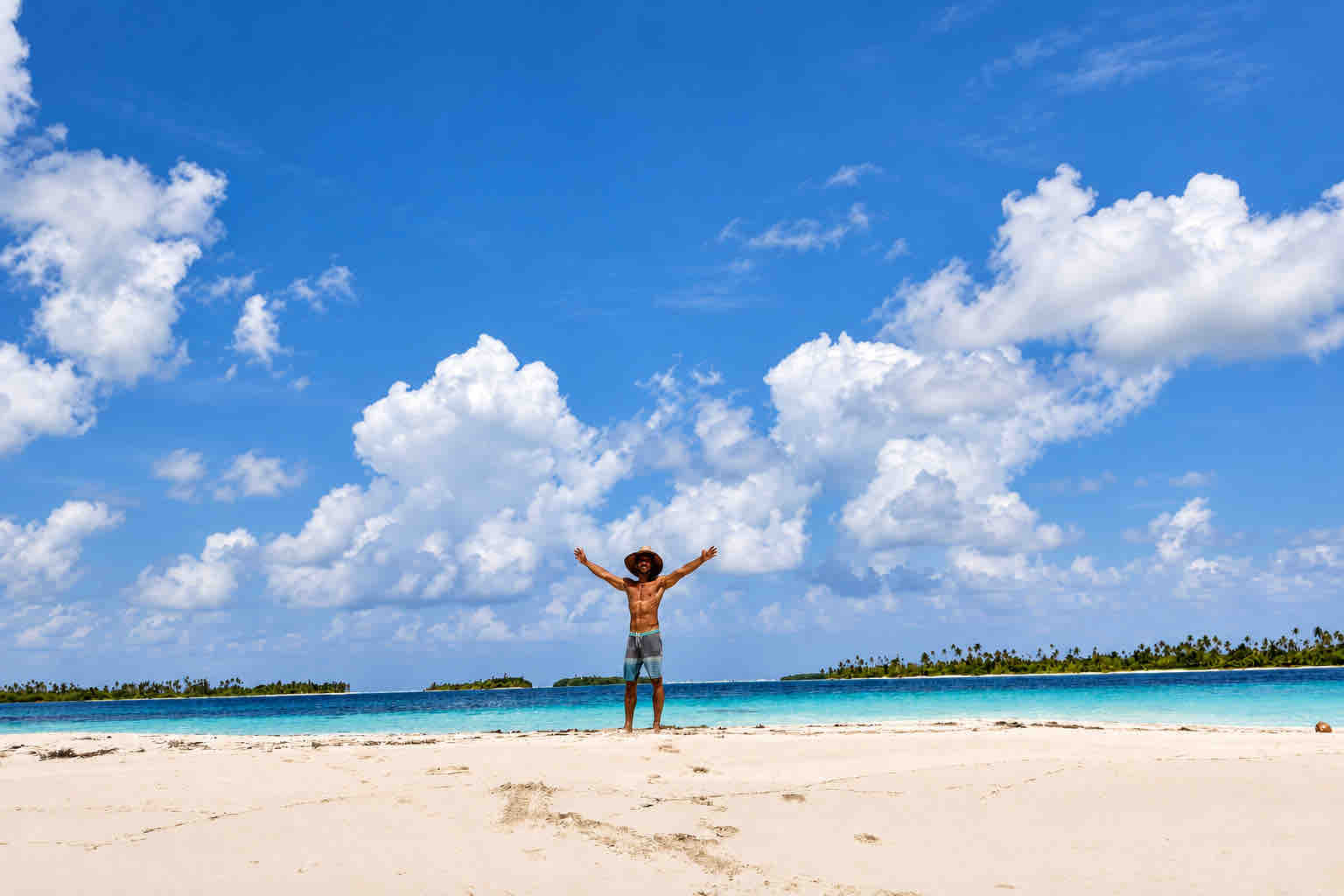 Traveler with arms outstretched on a white-sand islet in Cayos Holandeses, San Blas.