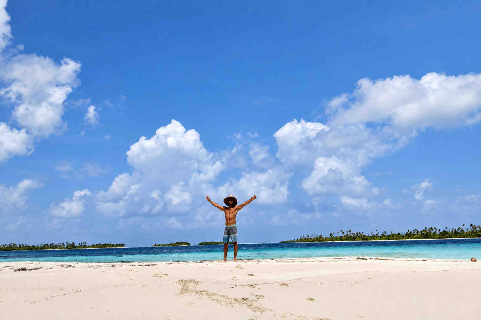 Visitor standing on a small white sand islet beneath a wide sky