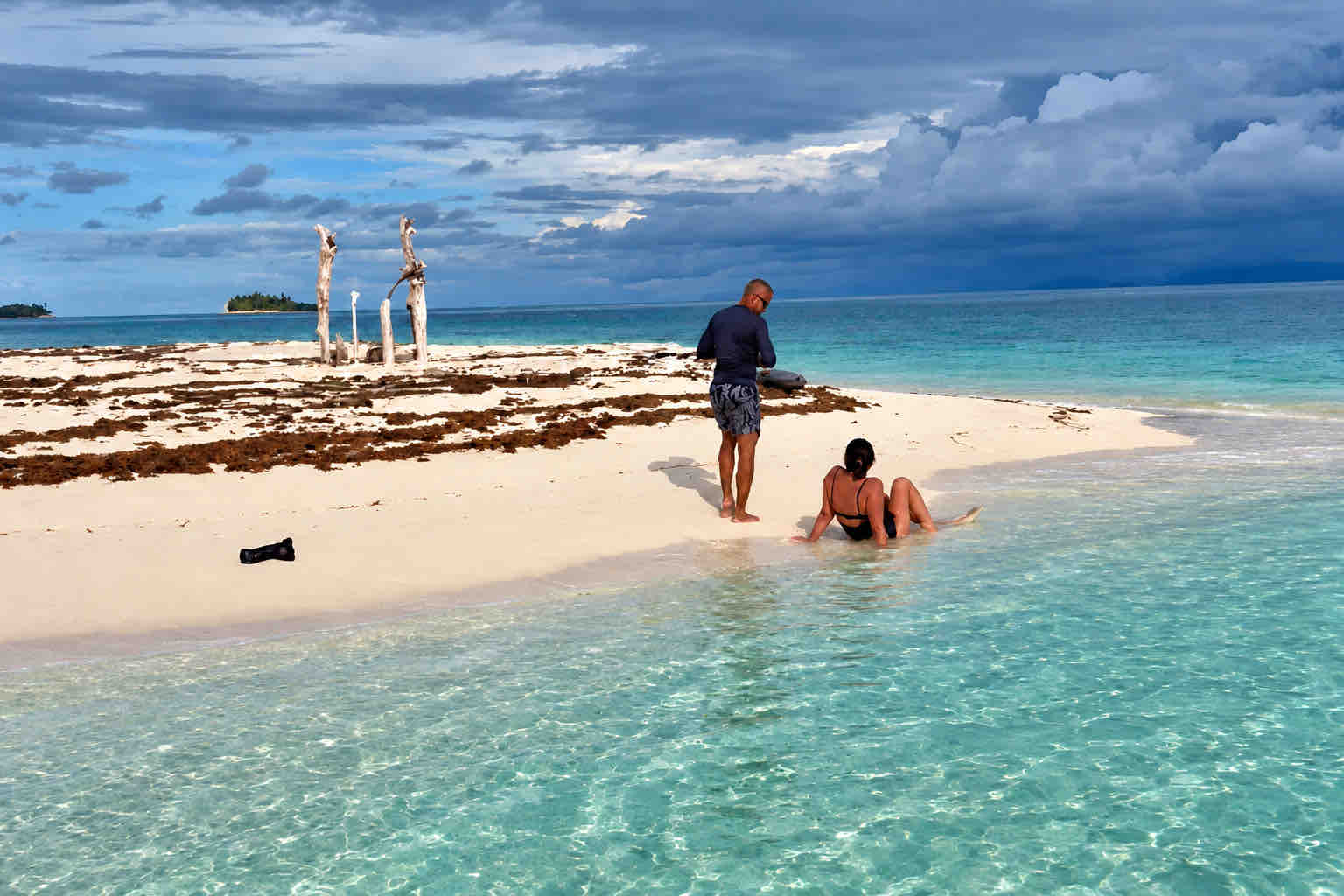 Two travelers relaxing on a Holandeses sandbar beside calm shallow water.