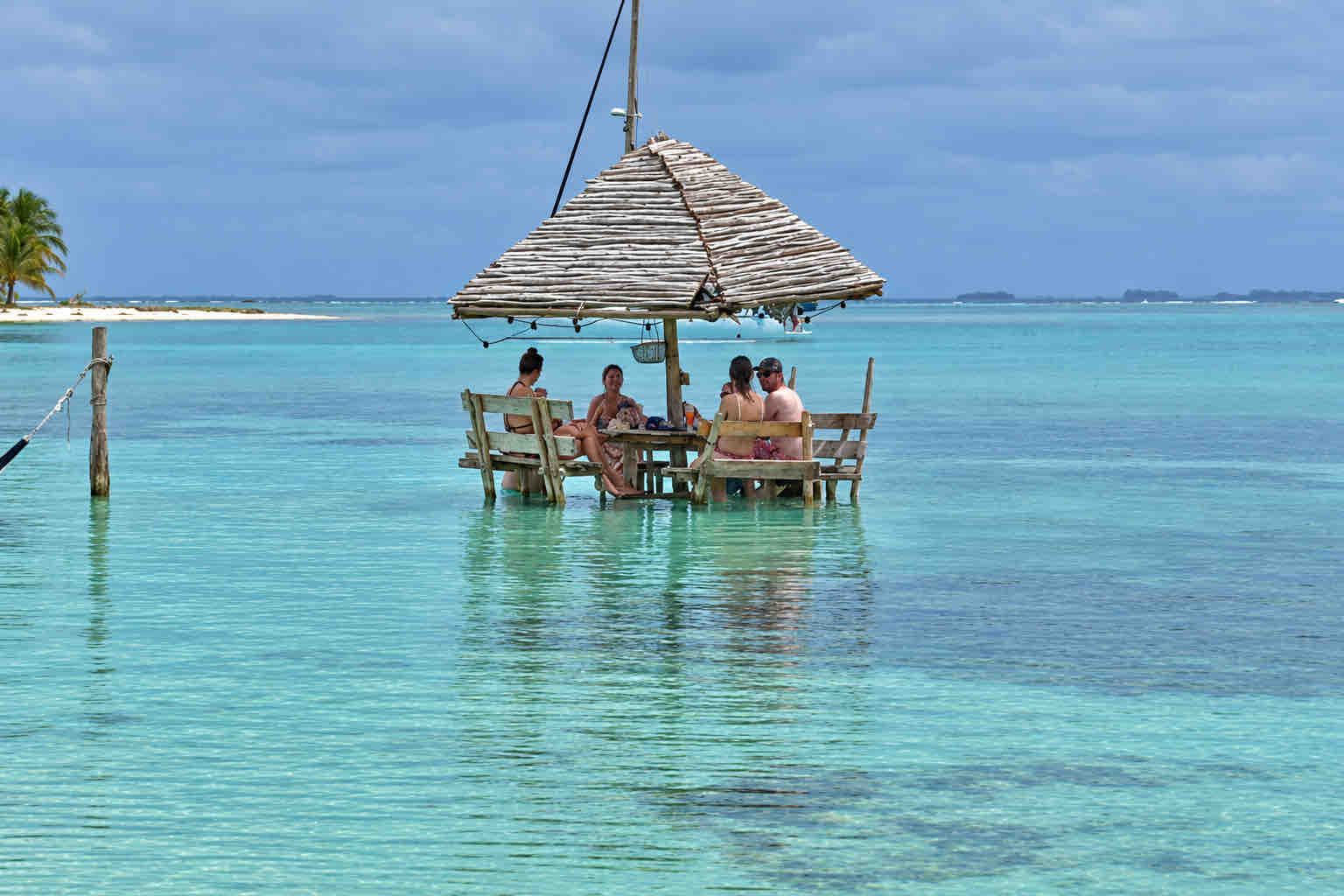 Guests seated at a shaded wooden table in shallow water in Holandeses, San Blas.