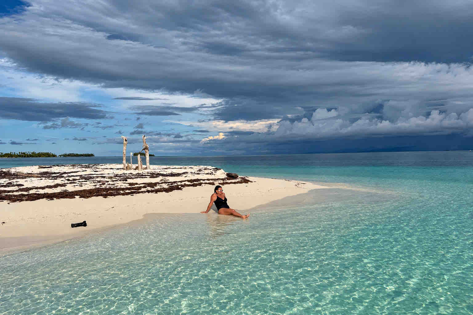Woman sitting at the waterline on a Holandeses sandbar beneath cloudy skies.