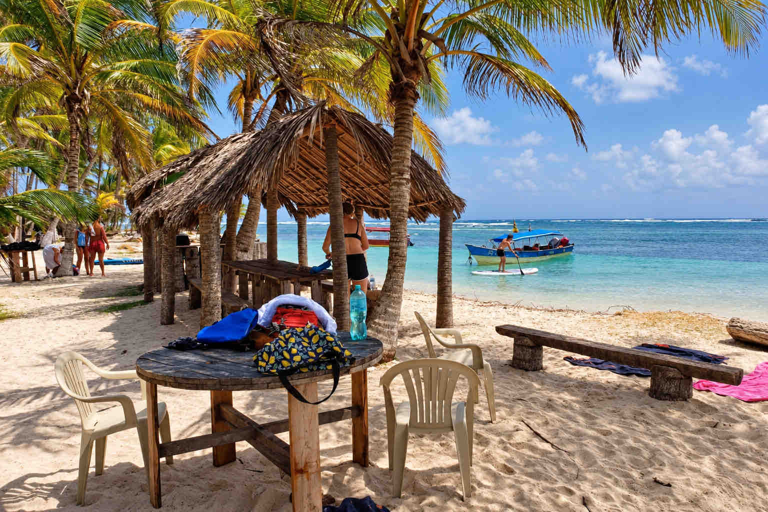 Thatched beach shelter, palm trees and a boat offshore in San Blas