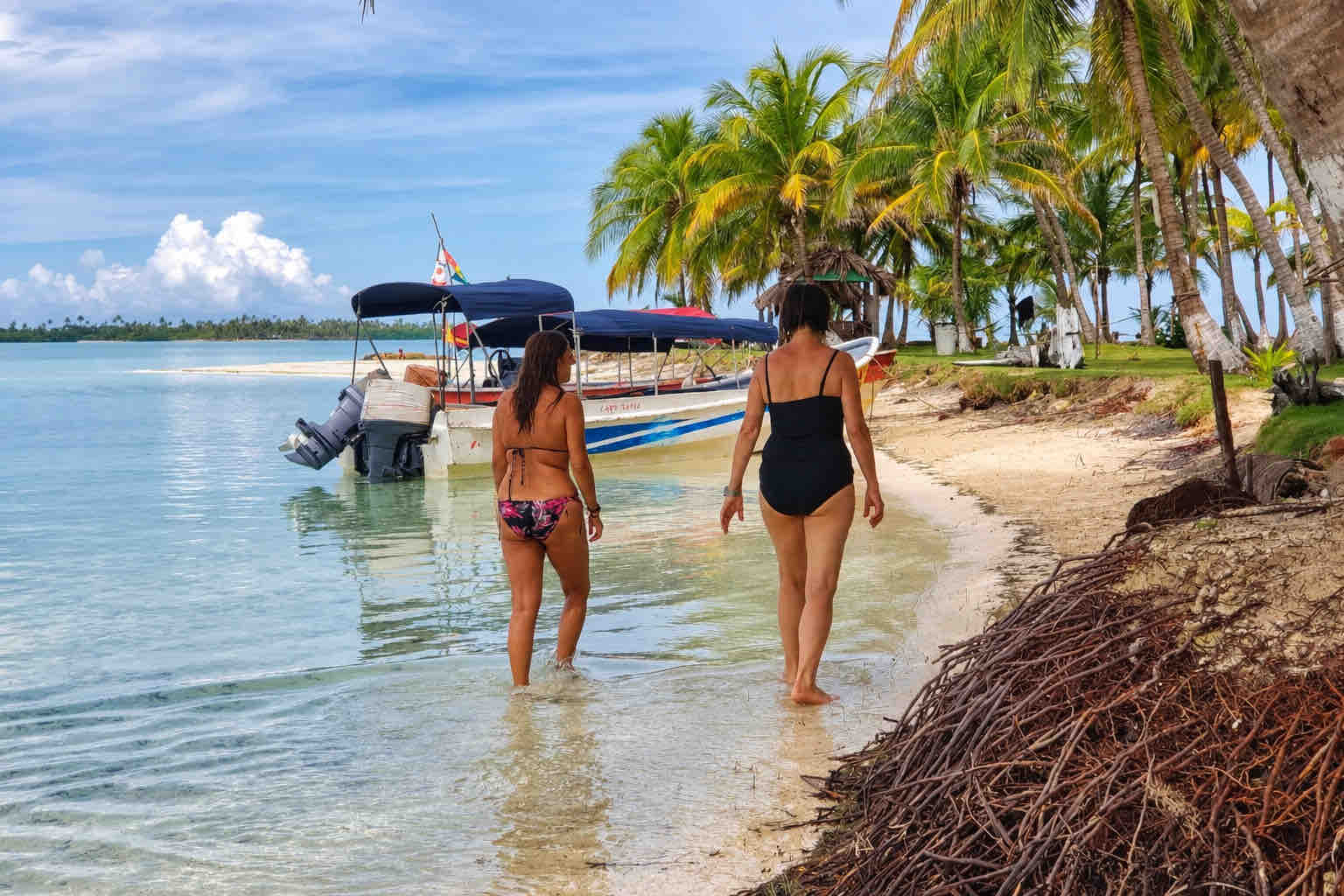 Two guests walking through shallow water beside a palm-lined San Blas shore