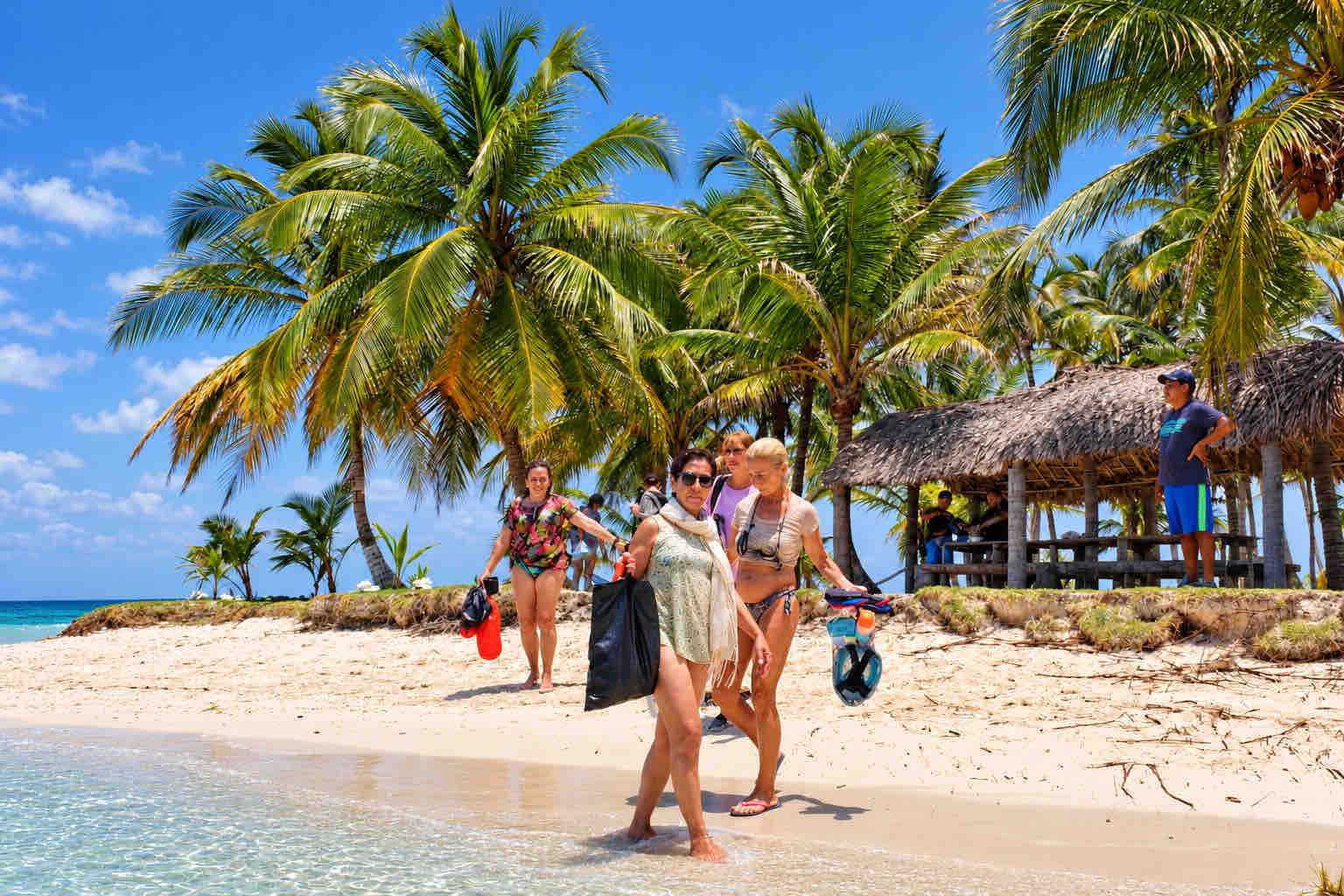 Travelers walking along a sandy beach beneath palm trees on a San Blas tour.