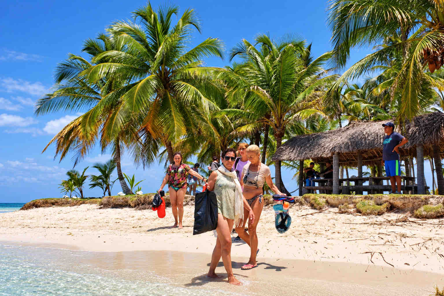 Tour guests walking on a sandy beach among palm trees in San Blas