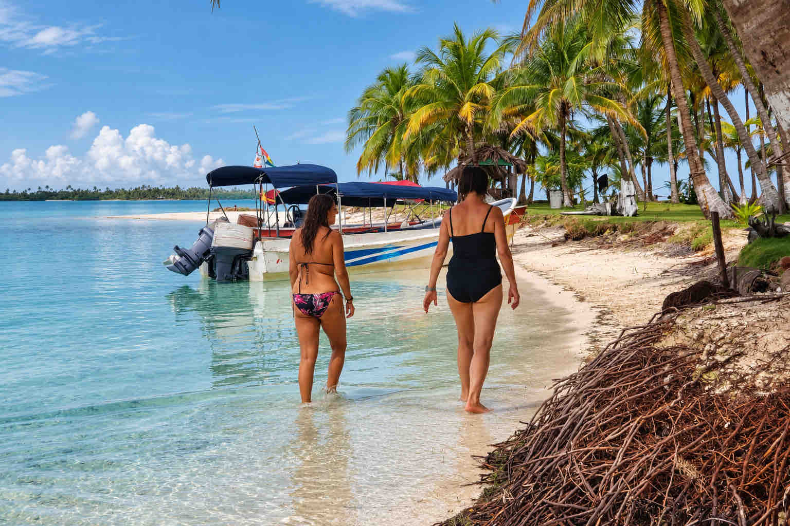 Two travelers walking through shallow water beside a boat on a San Blas tour.
