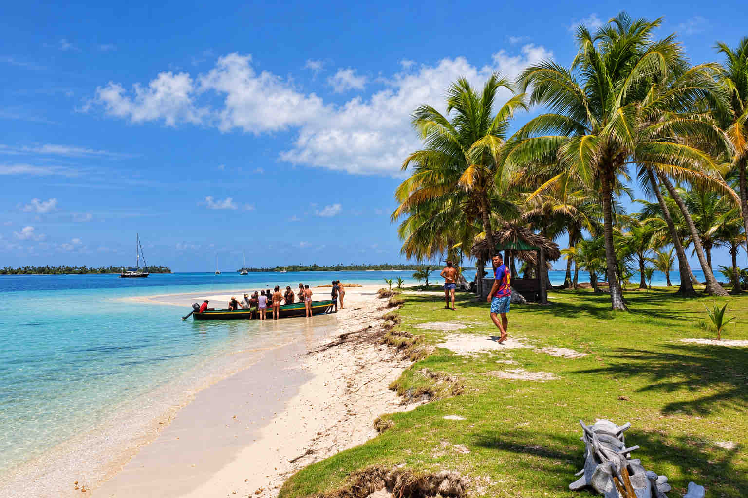 Travelers near a boat along a palm-lined island shore on a San Blas tour.